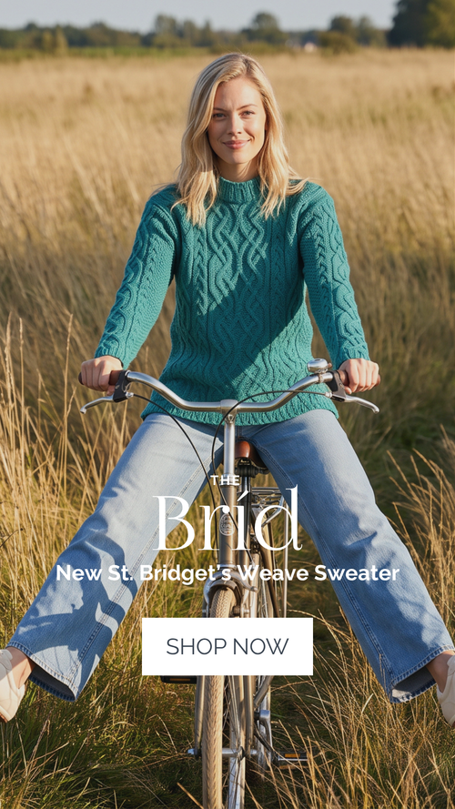 A woman riding a bicycle in a field of grass, wearing a teal cable-knit sweater and light blue jeans. Large text overlays read 'The Brid', 'New St.Bridgets weave Sweater