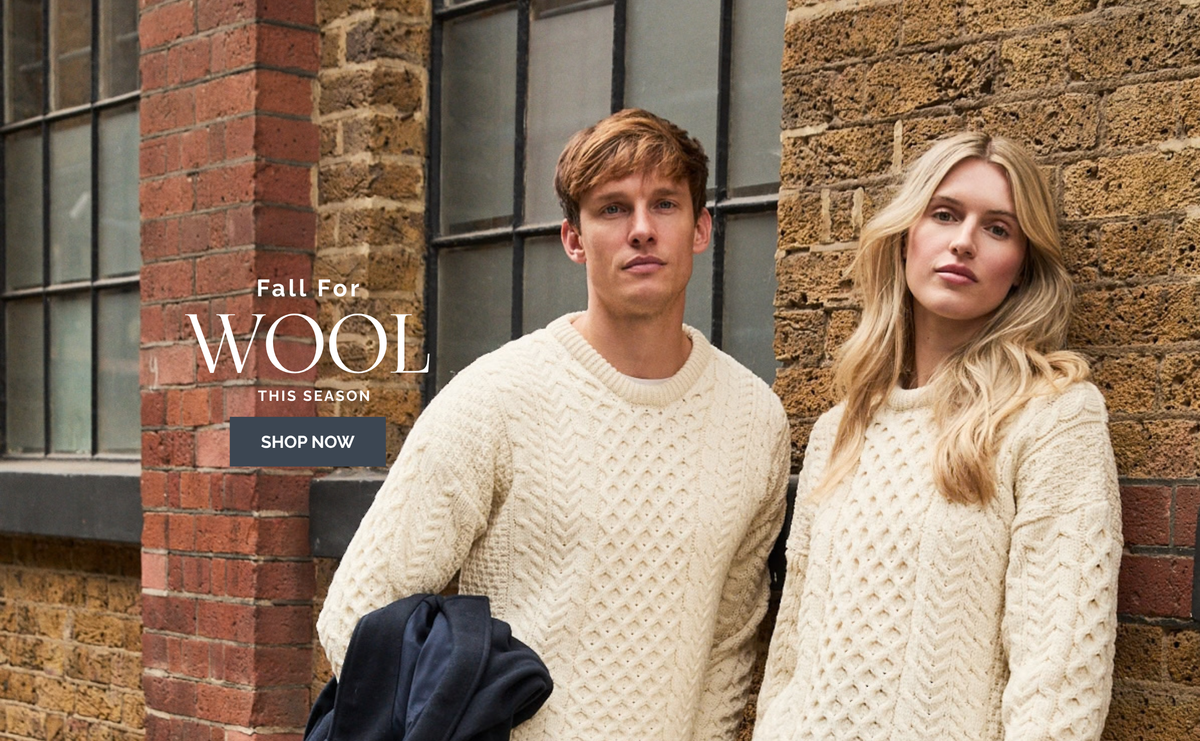 Two models wearing cream cable-knit Inisheer Aran wool sweaters standing against a brick wall, with a text overlay that reads 'Fall For WOOL THIS SEASON SHOP NOW'.